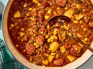Overhead view of a dutch oven of cowboy stew with a ladle and a cloth napkin all on a marble countertop