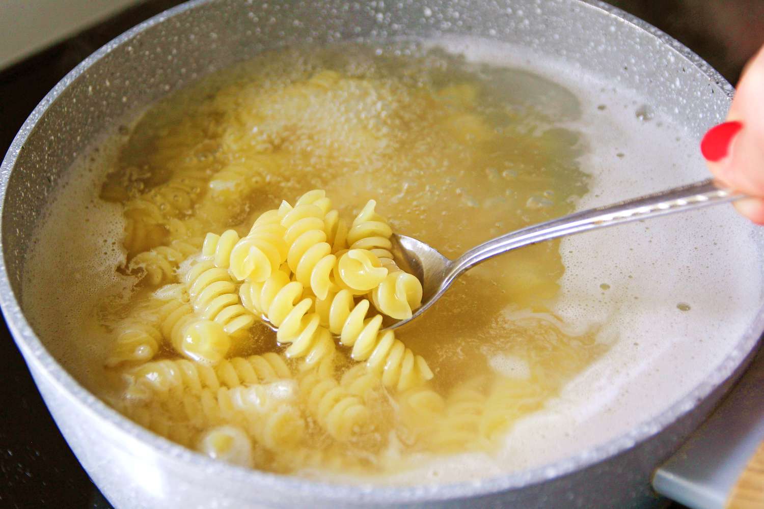 Pasta being boiled in water with a spoon lifting a portion of pasta