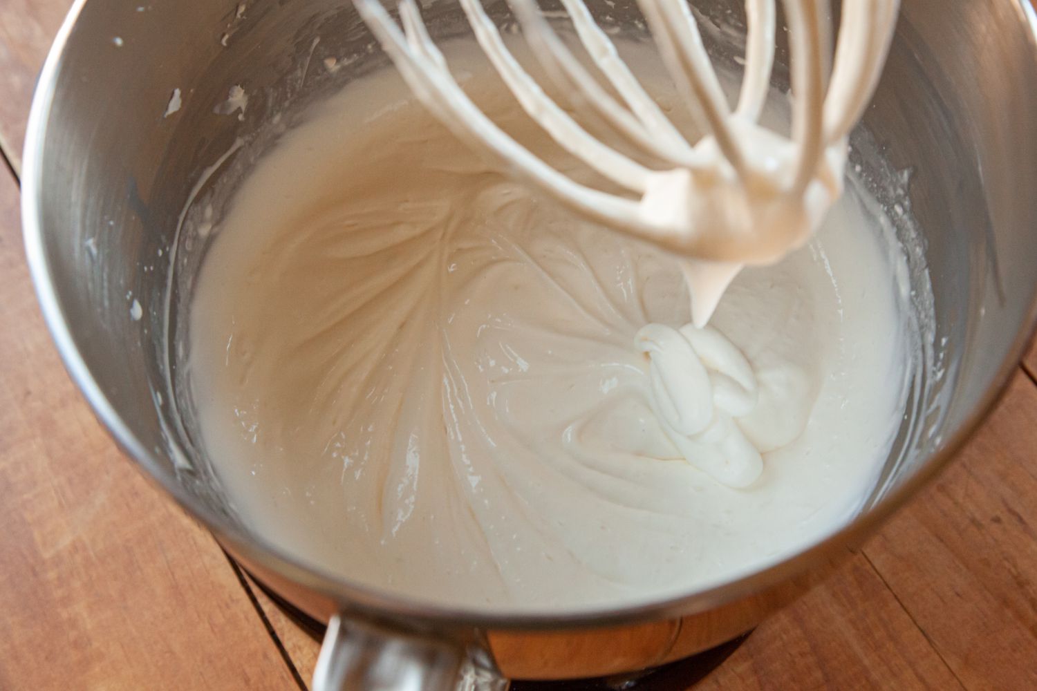 Overhead view of a stand mixer with a whisk attachment making a whipped cream frosting with cream cheese.