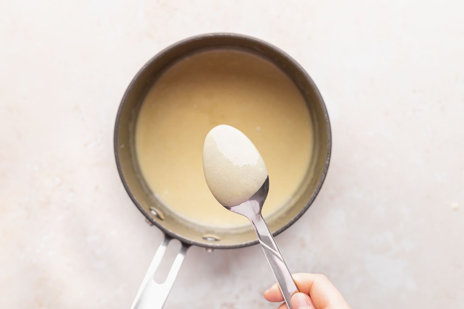 Spooning bread pudding sauce out of a saucepan.