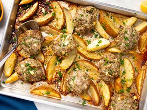 Baked meat patties and potato wedges on a tray garnished with herbs and seasoned