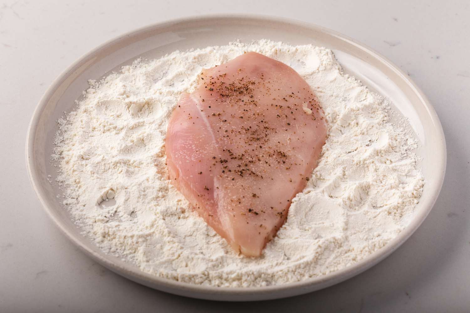 Chicken breast set in a plate with breading to make creamy chicken marsala.