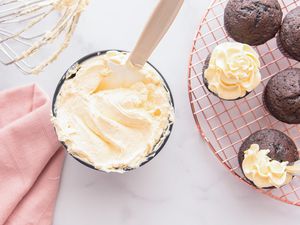 Creamy French buttercream frosting in a bowl with chocolate cupcakes to the right of it.