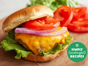 Cheeseburger with lettuce tomato and onion slices on a wooden board