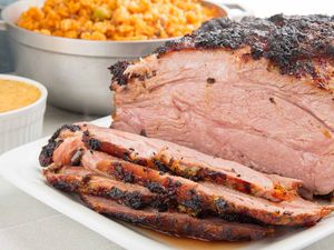 Caramelized mojo marinated pork roast with four juicy slices cut from it. A small white bowl of marinade rests next to a larger bowl of red rice.