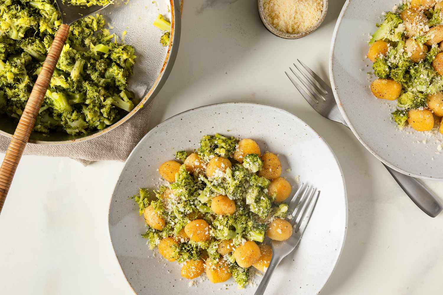 Plates of gnocchi with broccoli sauce and grated cheese served with forks