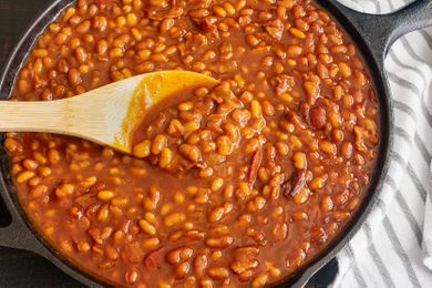 A skillet filled with baked beans being stirred with a wooden spoon