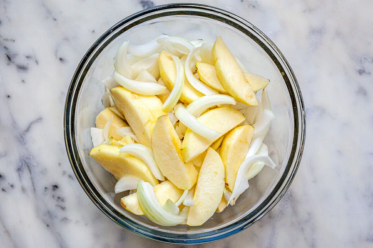 Sliced apples and onions in a glass bowl to make a pork shoulder recipe.