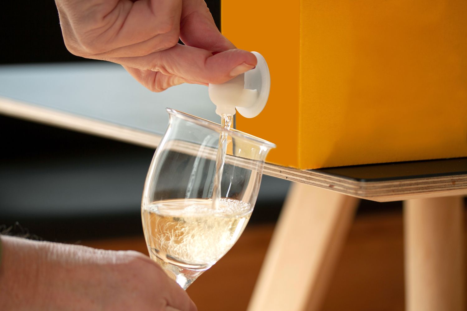Person pouring wine from a boxed wine dispenser into a wine glass