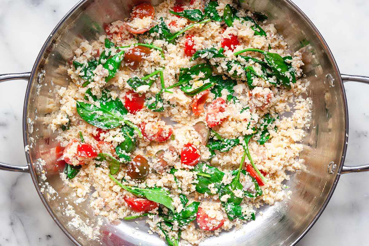 Cauliflower rice, spinach, basil and tomatoes in a high sided wok.