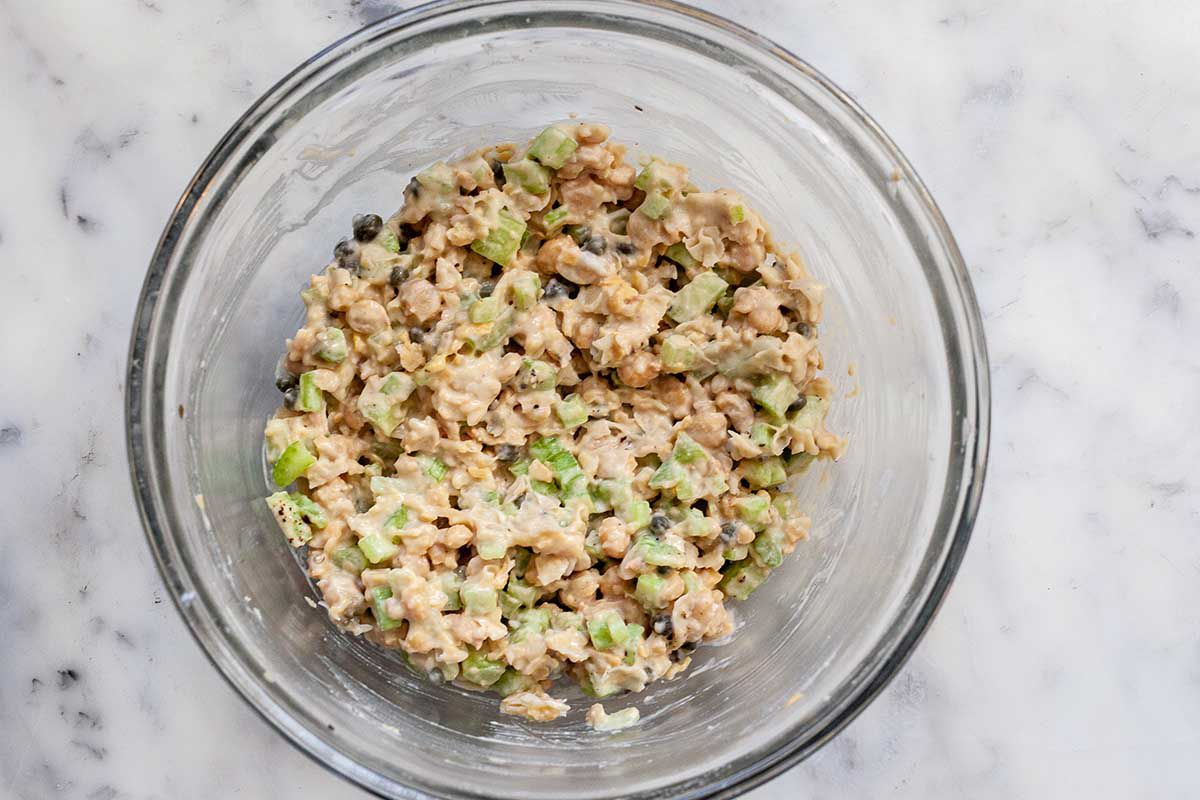 A glass mixing bowl is filled with vegetarian chickpea salad to make an easy sandwich recipe.