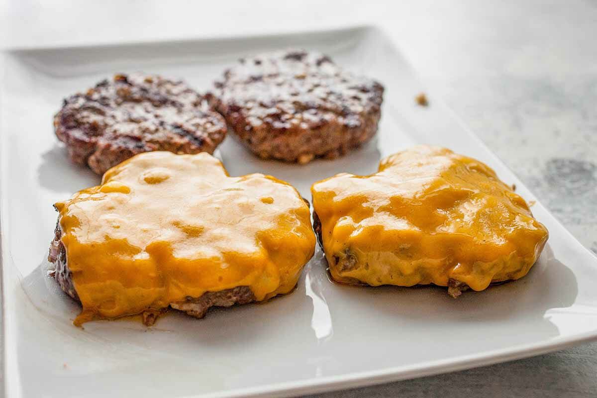 Two cheeseburger patties and two regular patties resting on a plate