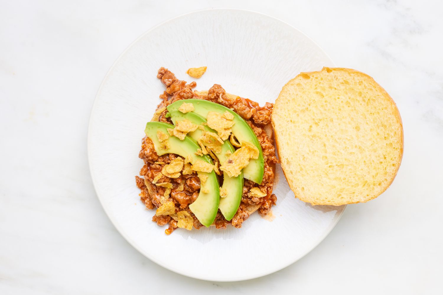 Chorizo sloppy joe assembled with sliced avocados and crushed Fritos chips on a plate