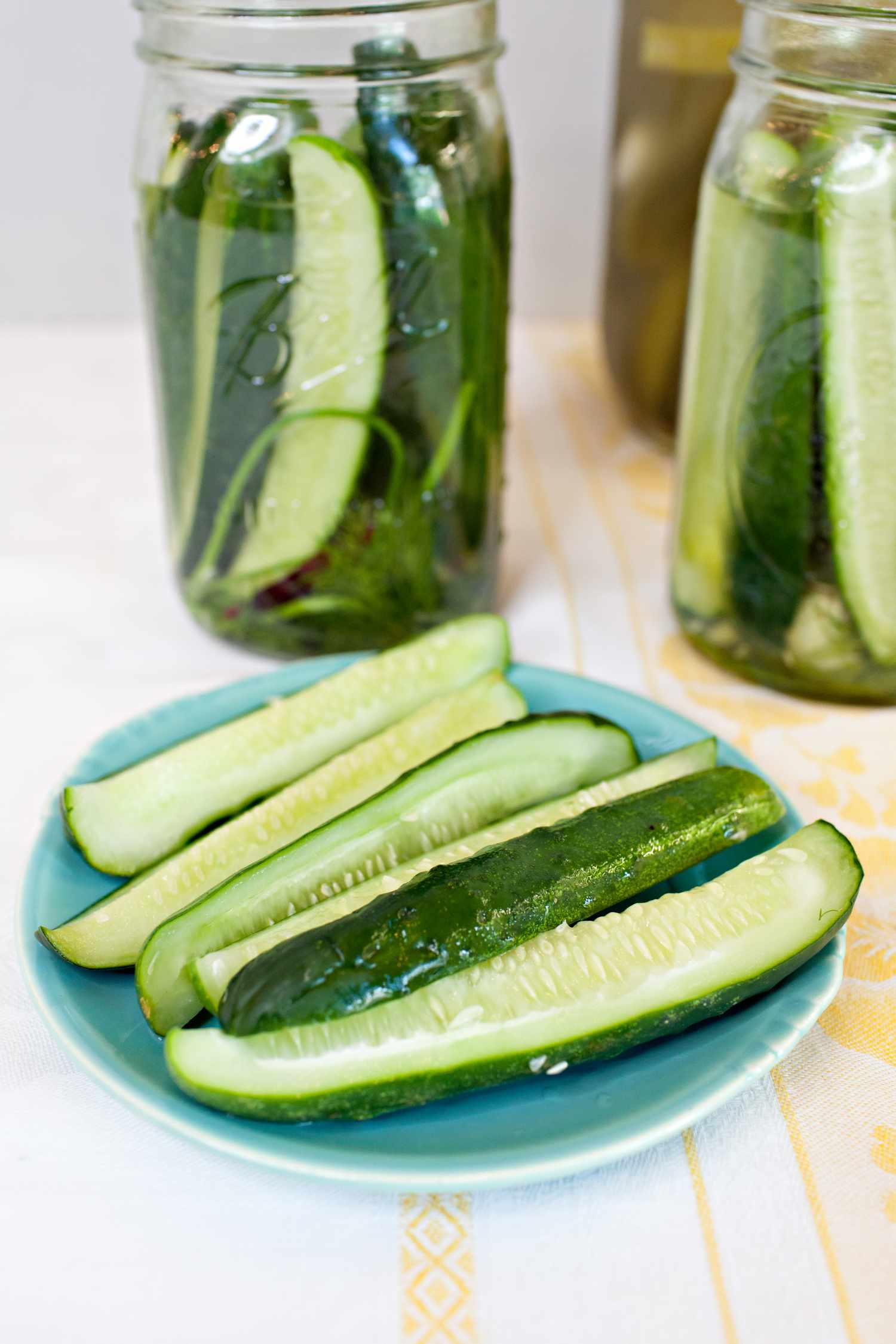 Fermented Pickles on a Small Plate with More in Jars in the Background