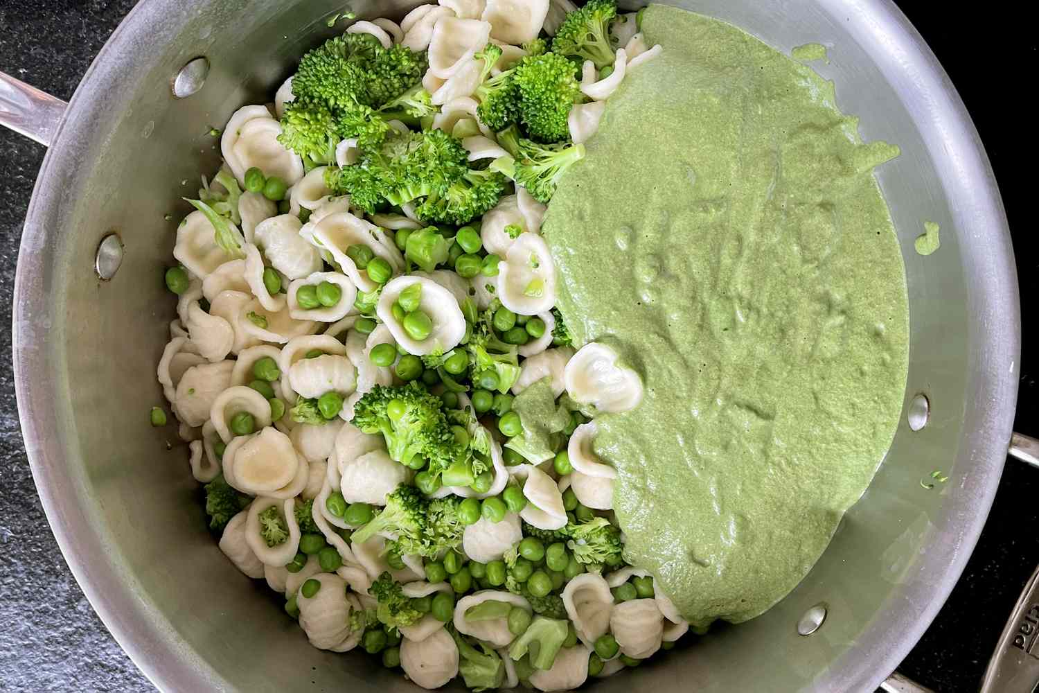 A pot containing orecchiette pasta broccoli florets green peas and green sauce
