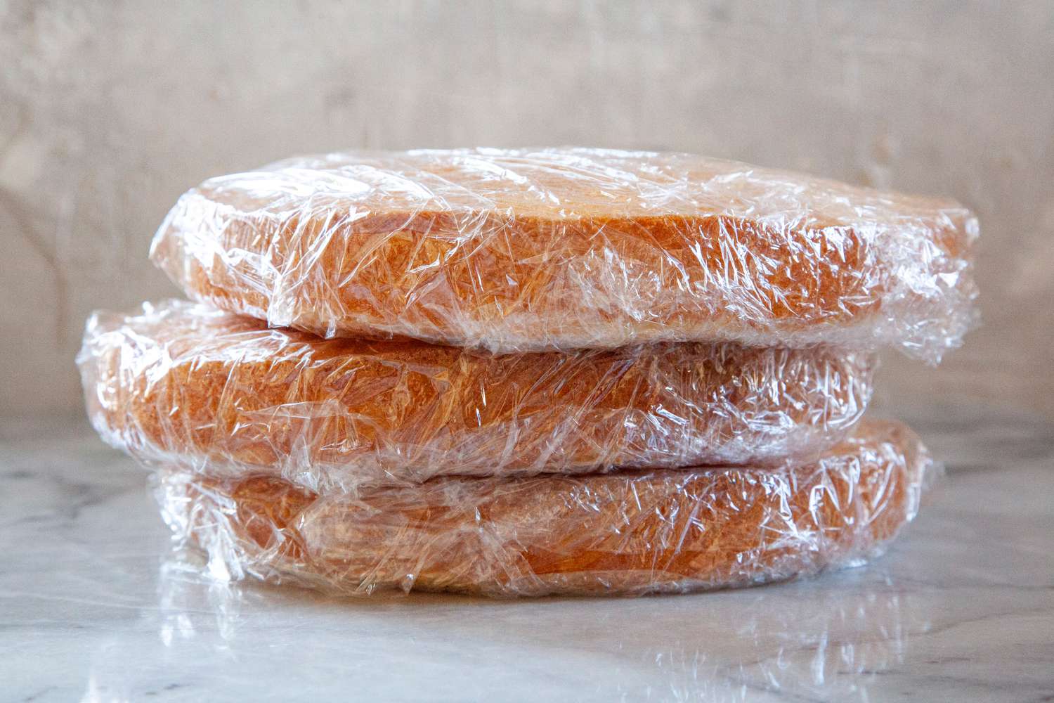 Three plastic wrapped cake layers to show how to freeze cake.