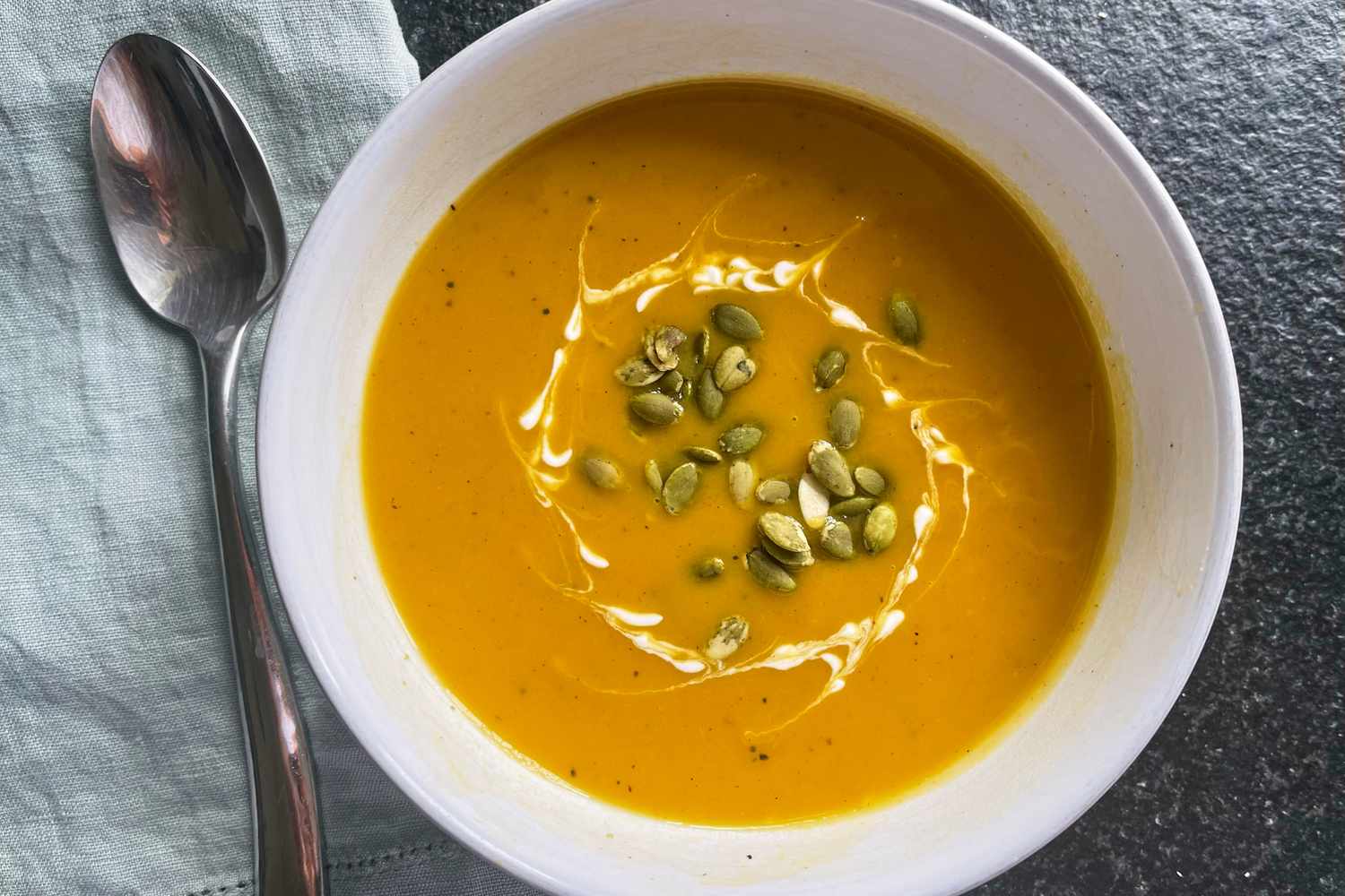 A bowl of butternut squash soup topped with seeds and a swirl of cream