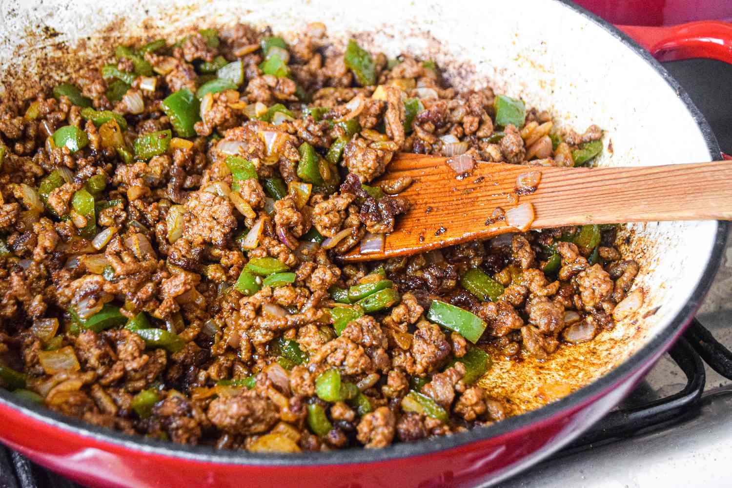A pan cooking ground beef, chopped bell peppers, and onions