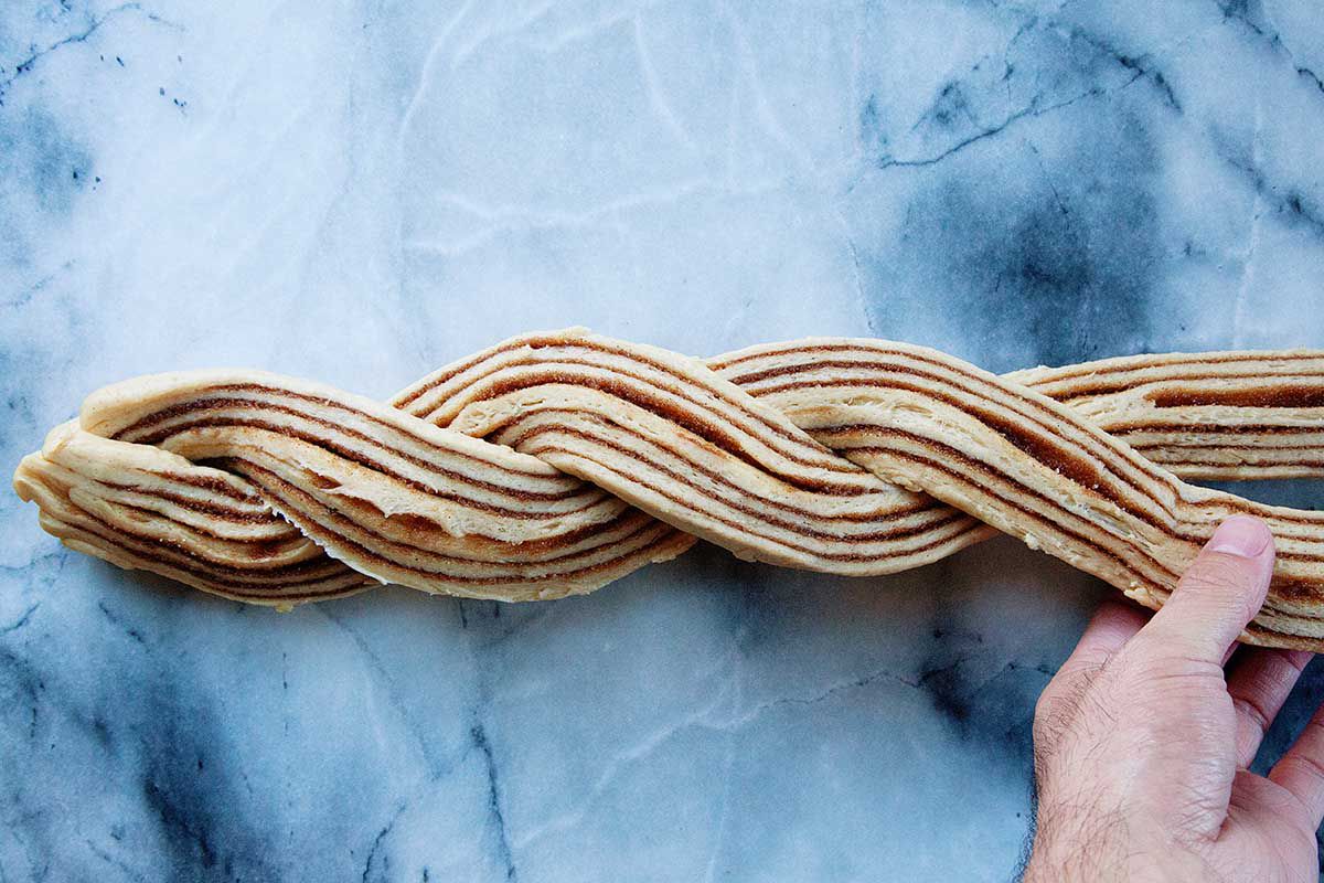 The halved homemade King Cake dough is being twisted on a marble background.