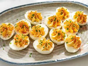 A ceramic serving plate with million dollar deviled eggs, garnished with chopped chives and paprika