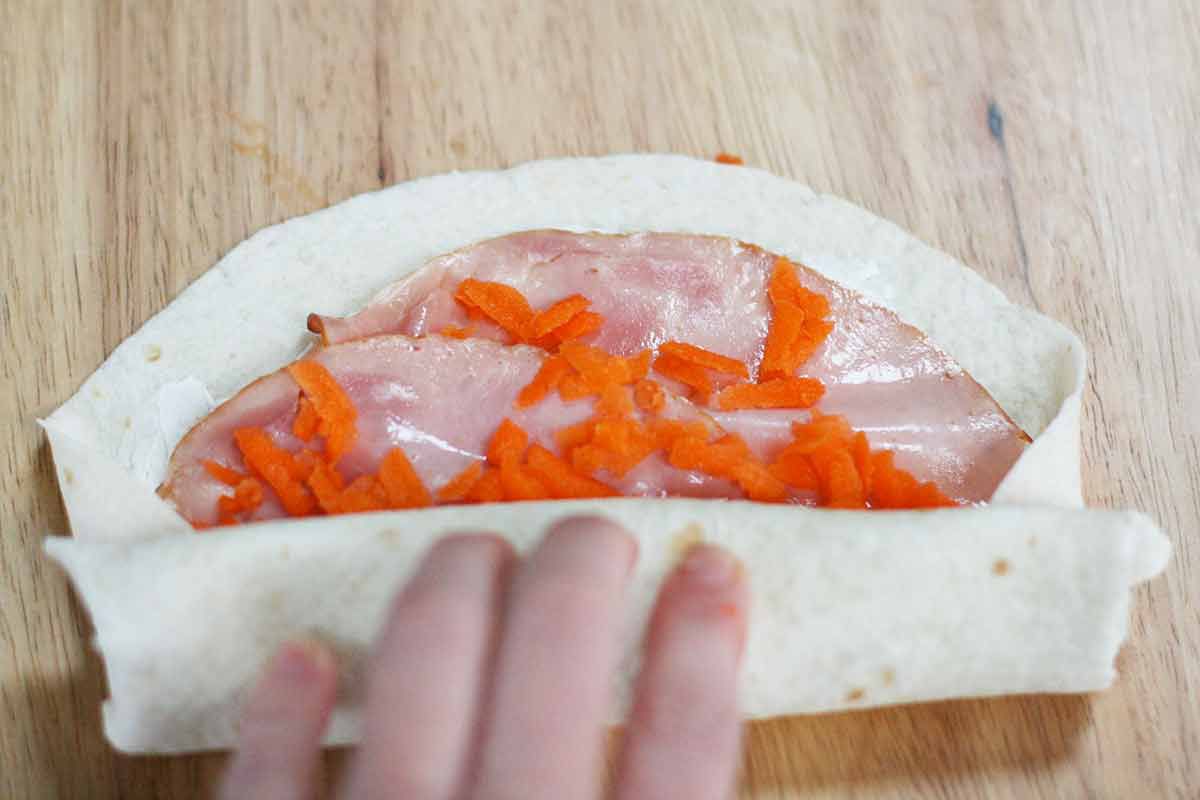 A ham and carrot wrap for kids, served on a flour tortilla