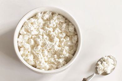 A bowl filled with cottage cheese next to a spoon containing some of the cheese