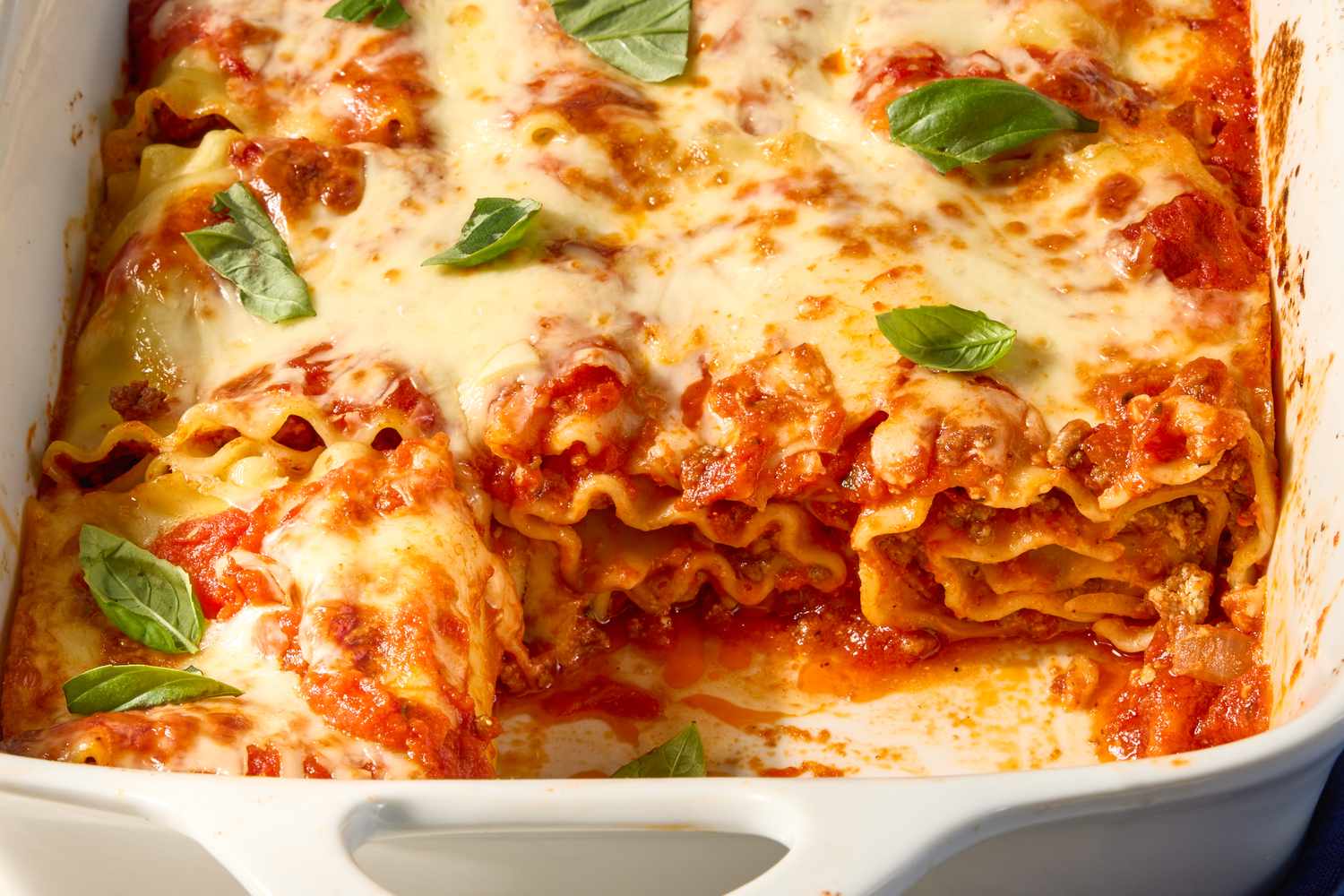 A baking dish with lasagna rollups topped with melted cheese and basil leaves