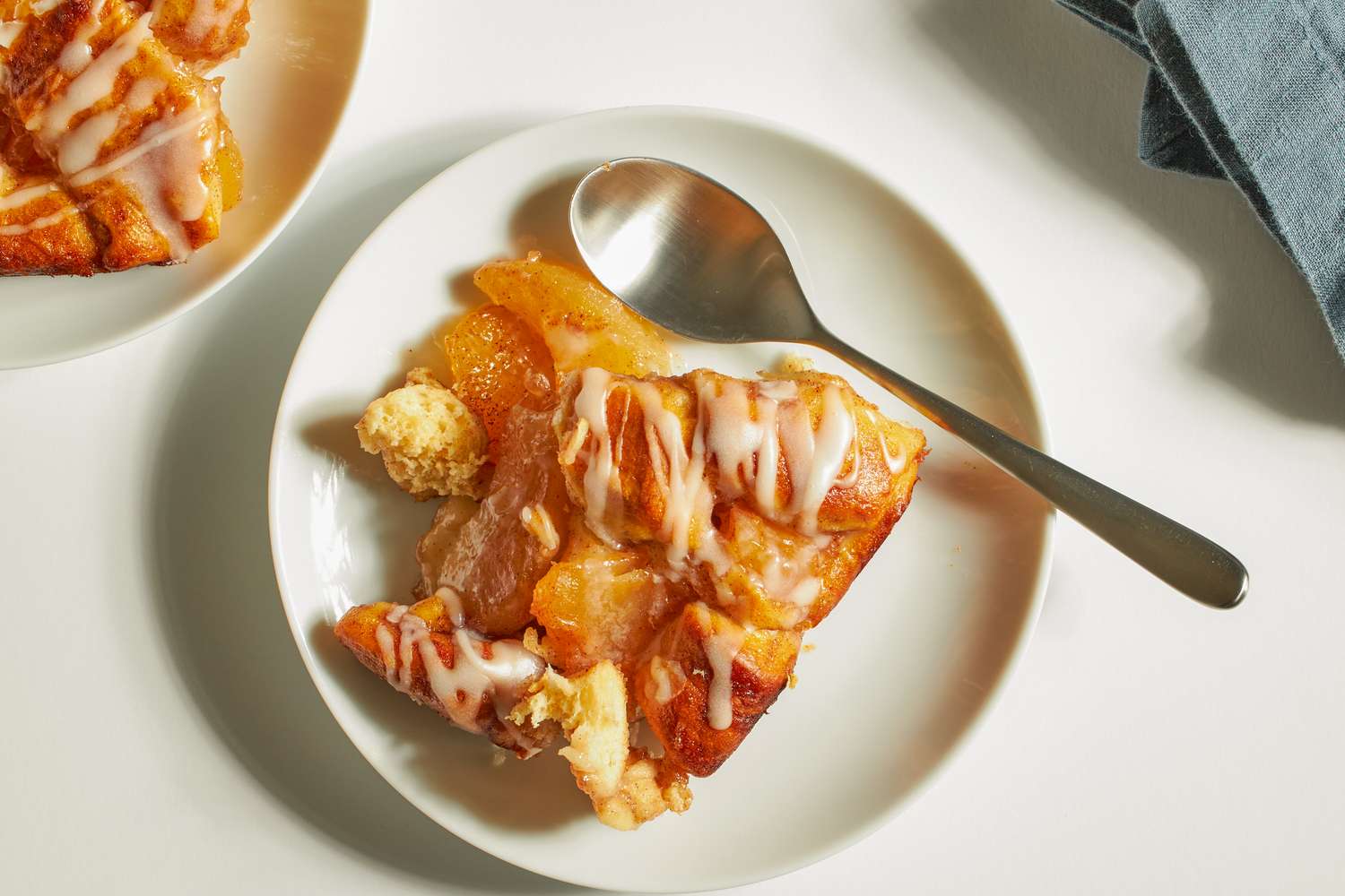 A plate with a serving of apple cinnamon cobbler topped with icing and a spoon beside it