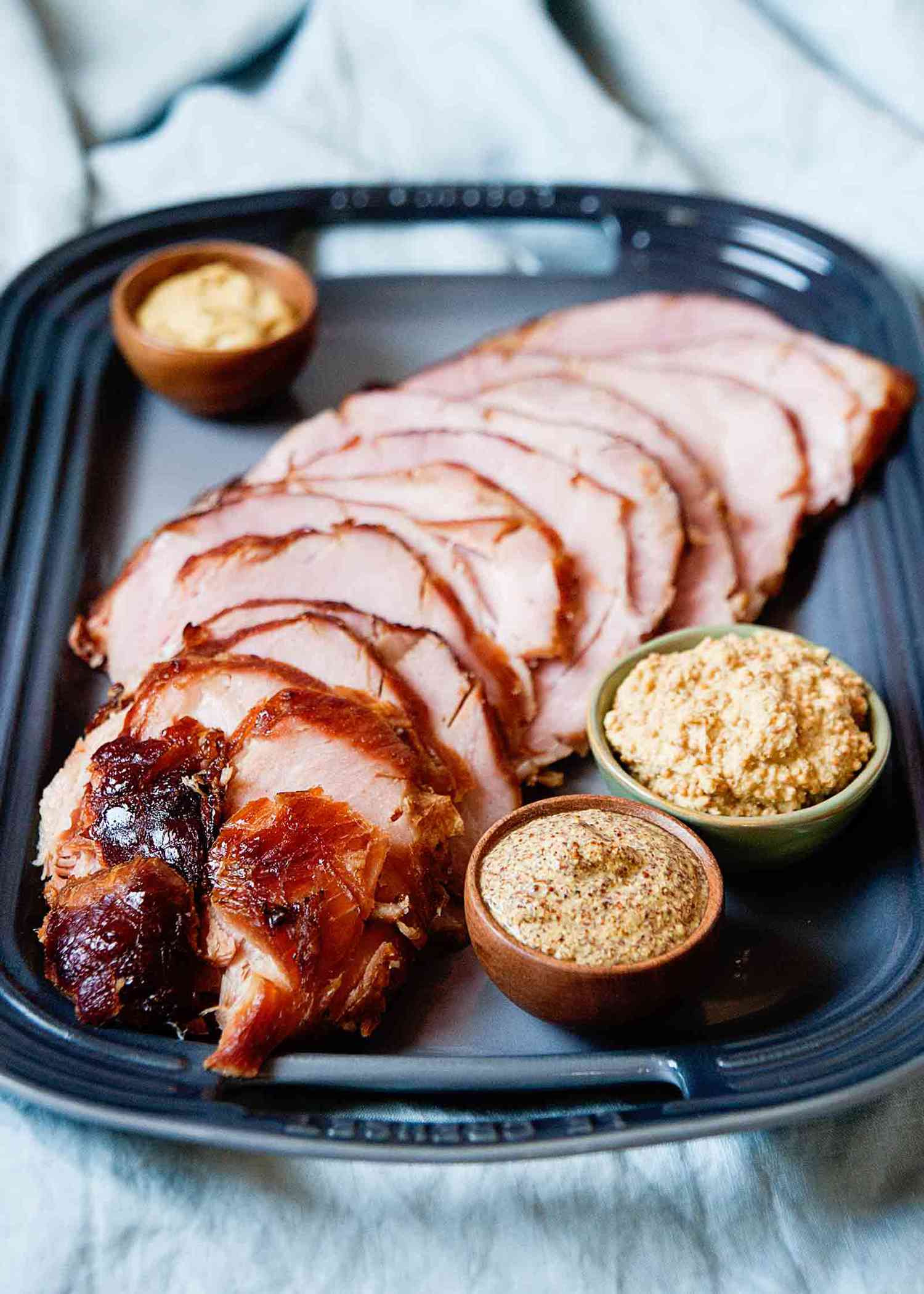 How to Bake a Ham Bone-In - sliced ham on platter with small bowls of mustard