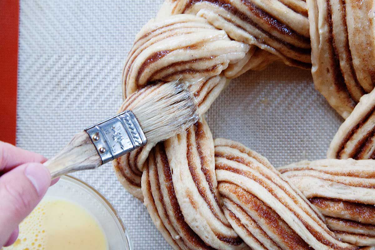The risen King Cake dough is being brushed with melted butter with a pastry brush.