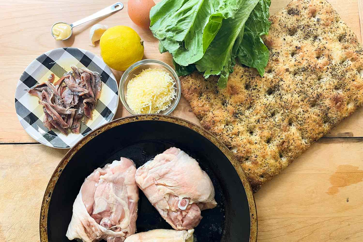 Ingredients for a sandwich including chicken lettuce bread lemon Parmesan anchovies and garlic displayed on a wooden surface