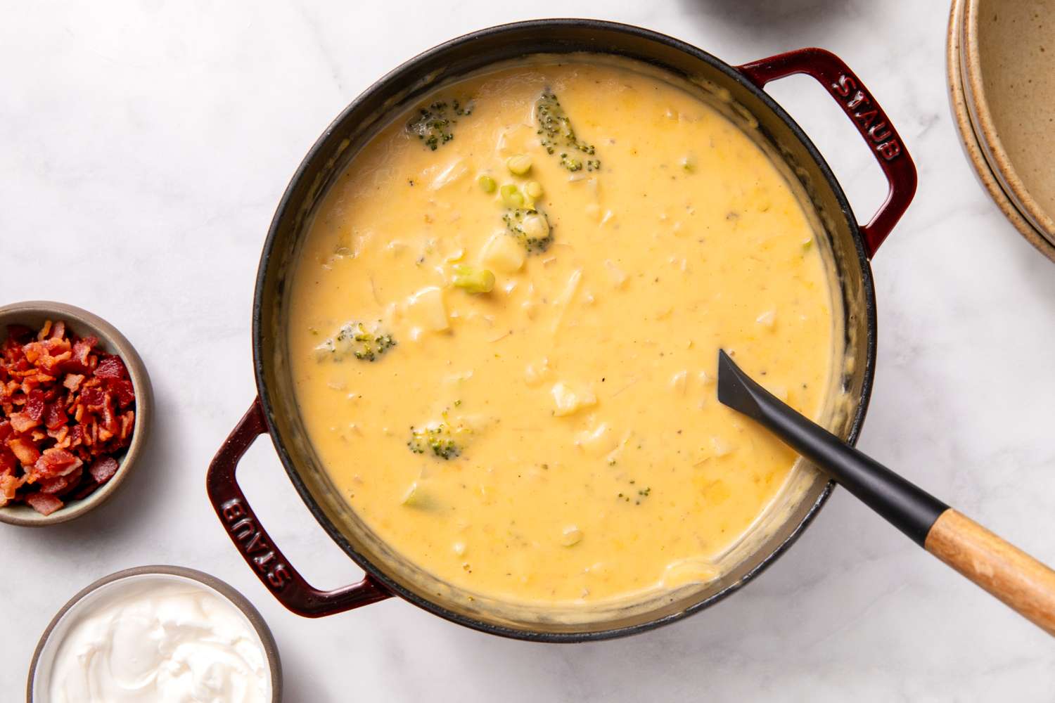 Broccoli potato soup in a pot with a ladle served with toppings on the side