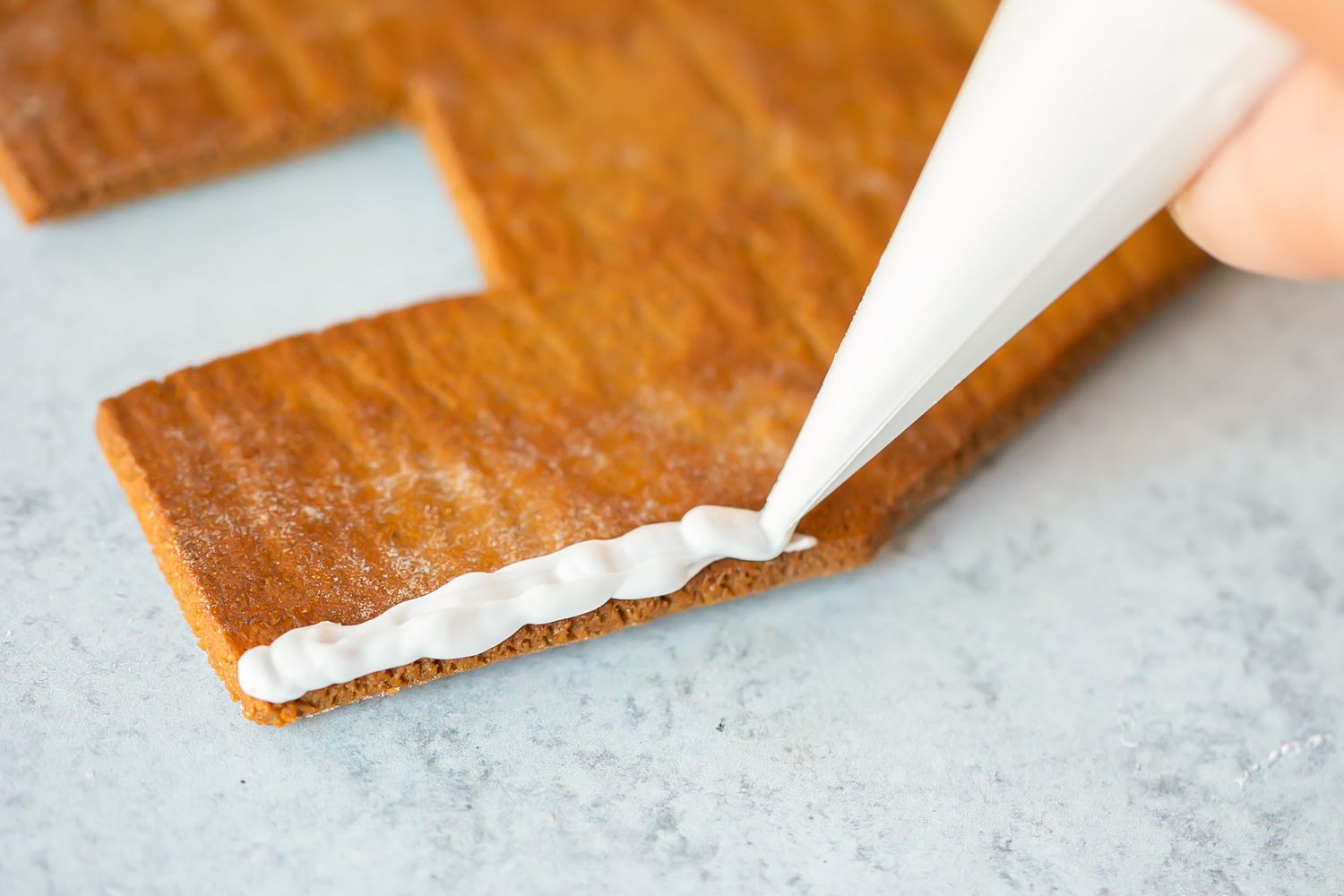 Piping royal icing on gingerbread to show how to make a gingerbread house.