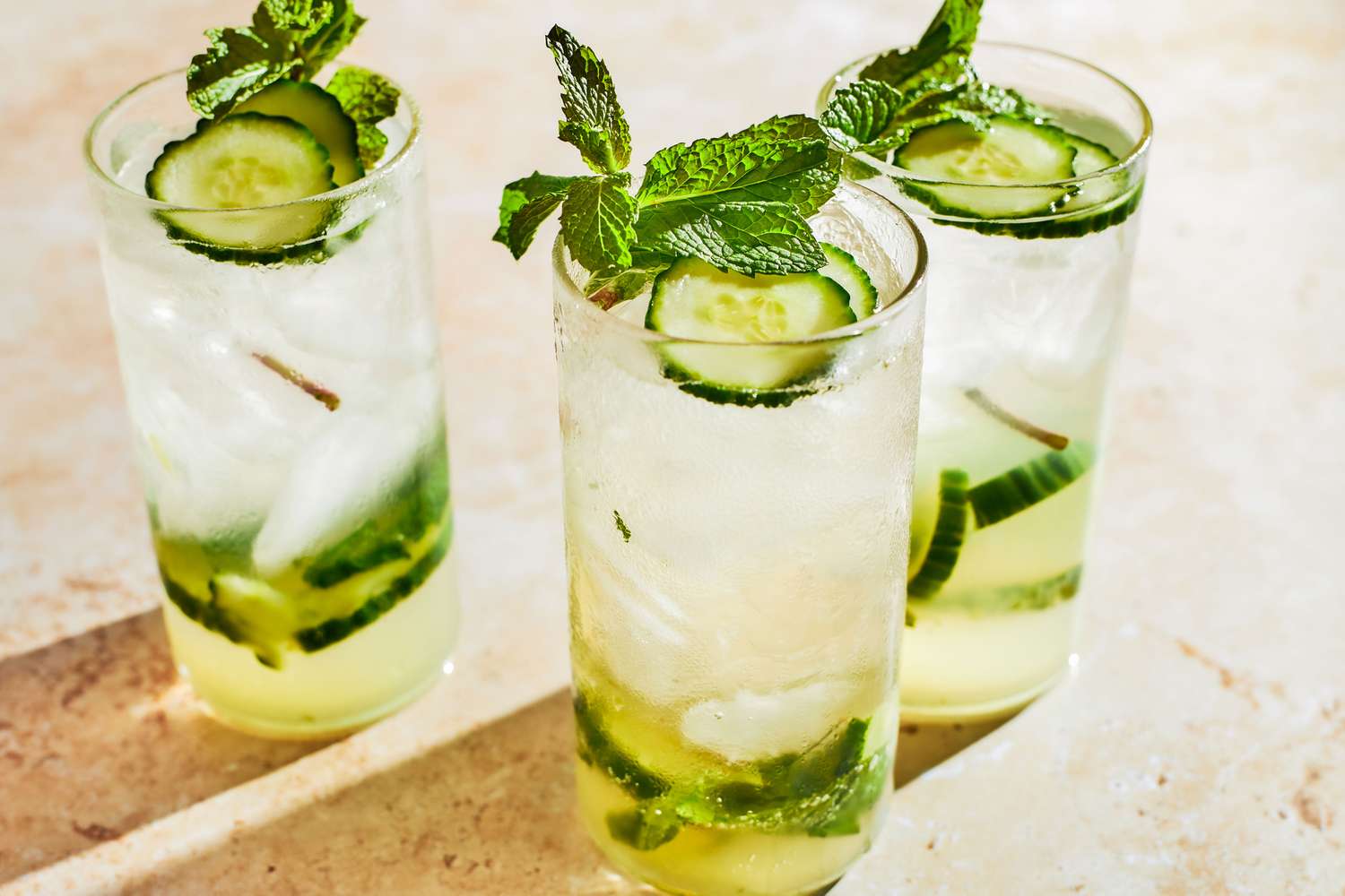 3 cocktail glasses filled with 3-Ingredient Mocktail, garnished with cucumber slices and mint leaves