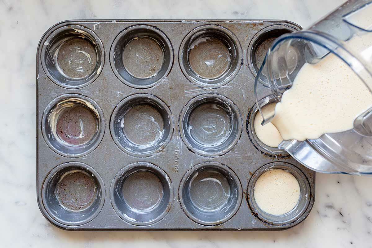 Pouring popover batter into a greased muffin tin for a popover recipe.