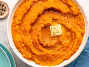 Overhead view of a white bowl of butternut squash topped with butter ad spices resting on a blue table napkin