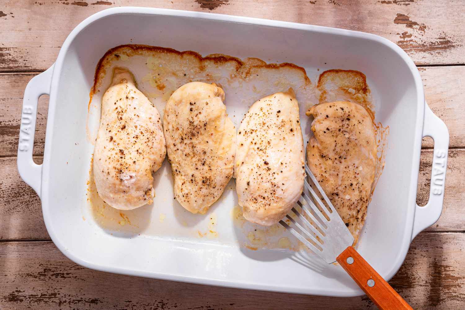 Baked chicken breast in a casserole dish with one piece slightly lifted using a spatula 
