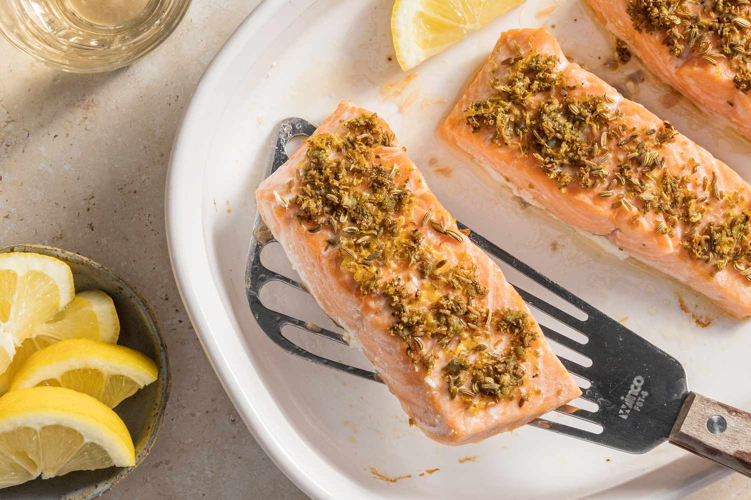 4-ingredient mediterranean salmon on a platter next to a bowl of lemon wedges and a glass of wine 