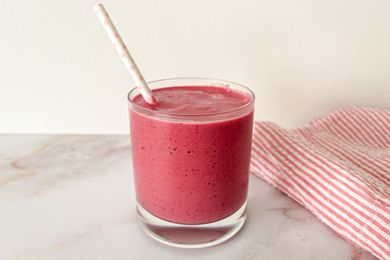 A short glass filled with a pink smoothie and a white paper straw with light pink polka dots