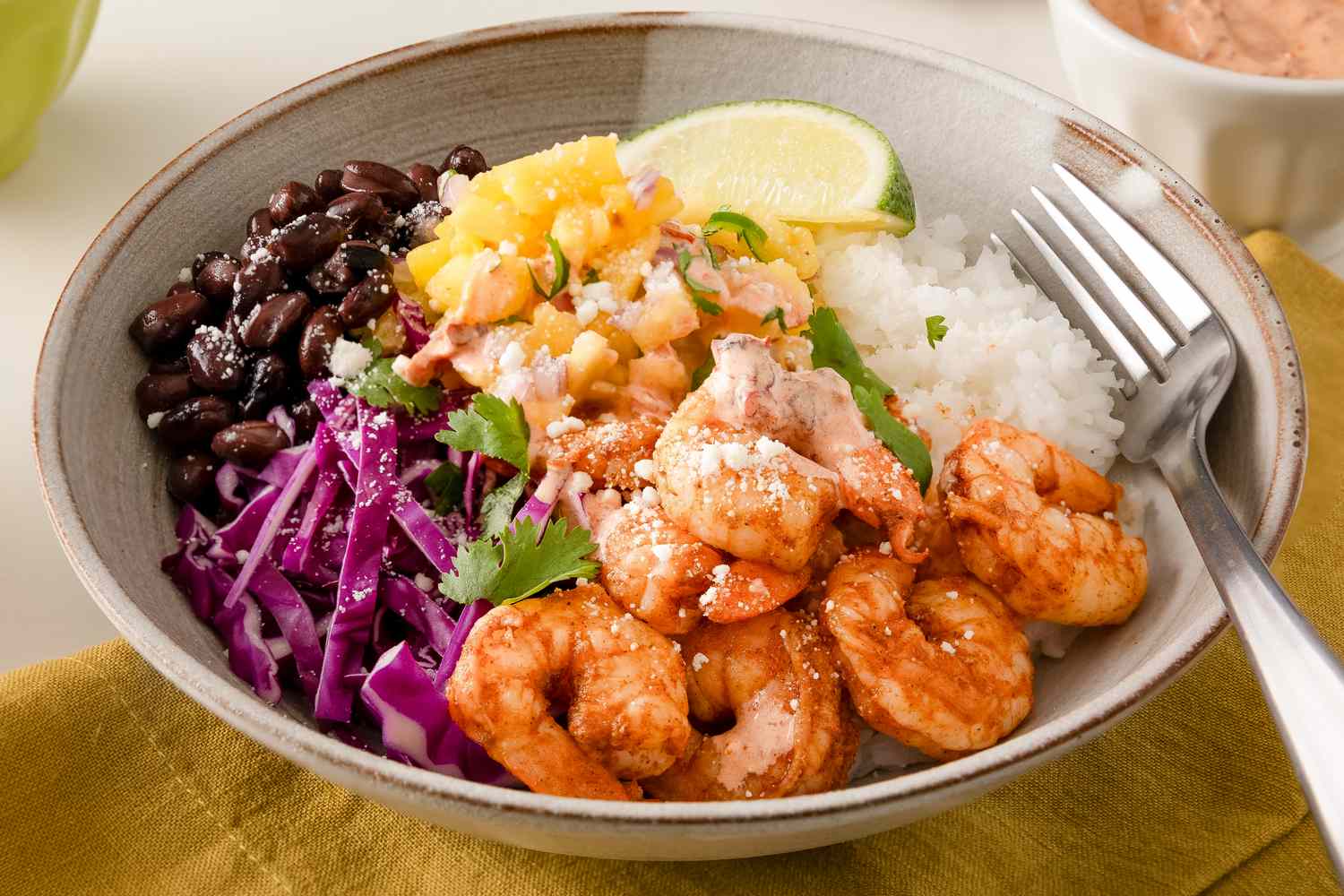 A Cajun shrimp bowl with rice, beans, pickled cabbage, and mixed toppings, served with a lime wedge and fork