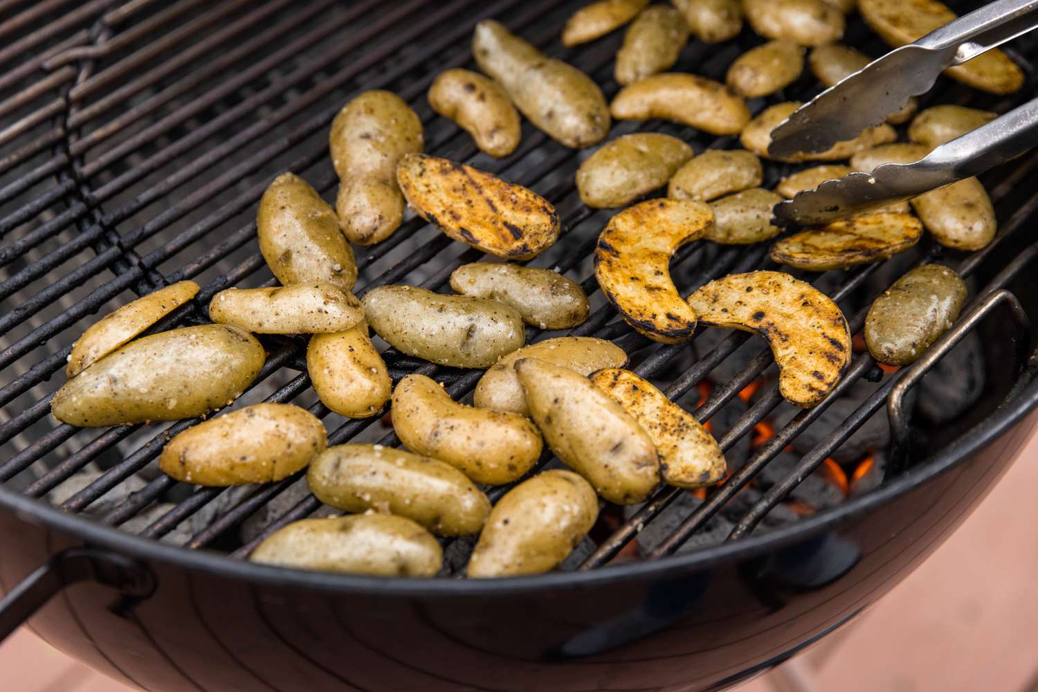 Grilled Potatoes Flipped on the Grill Using a Set of Tongs