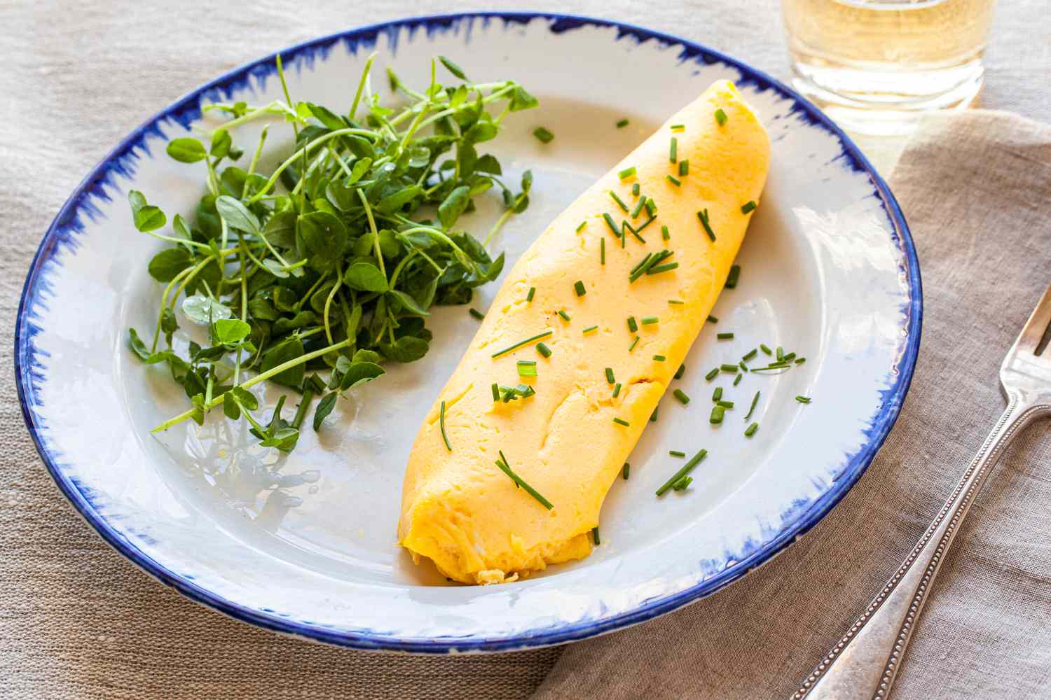 French Omelette with Greens on Plate Next to Fork and Glass