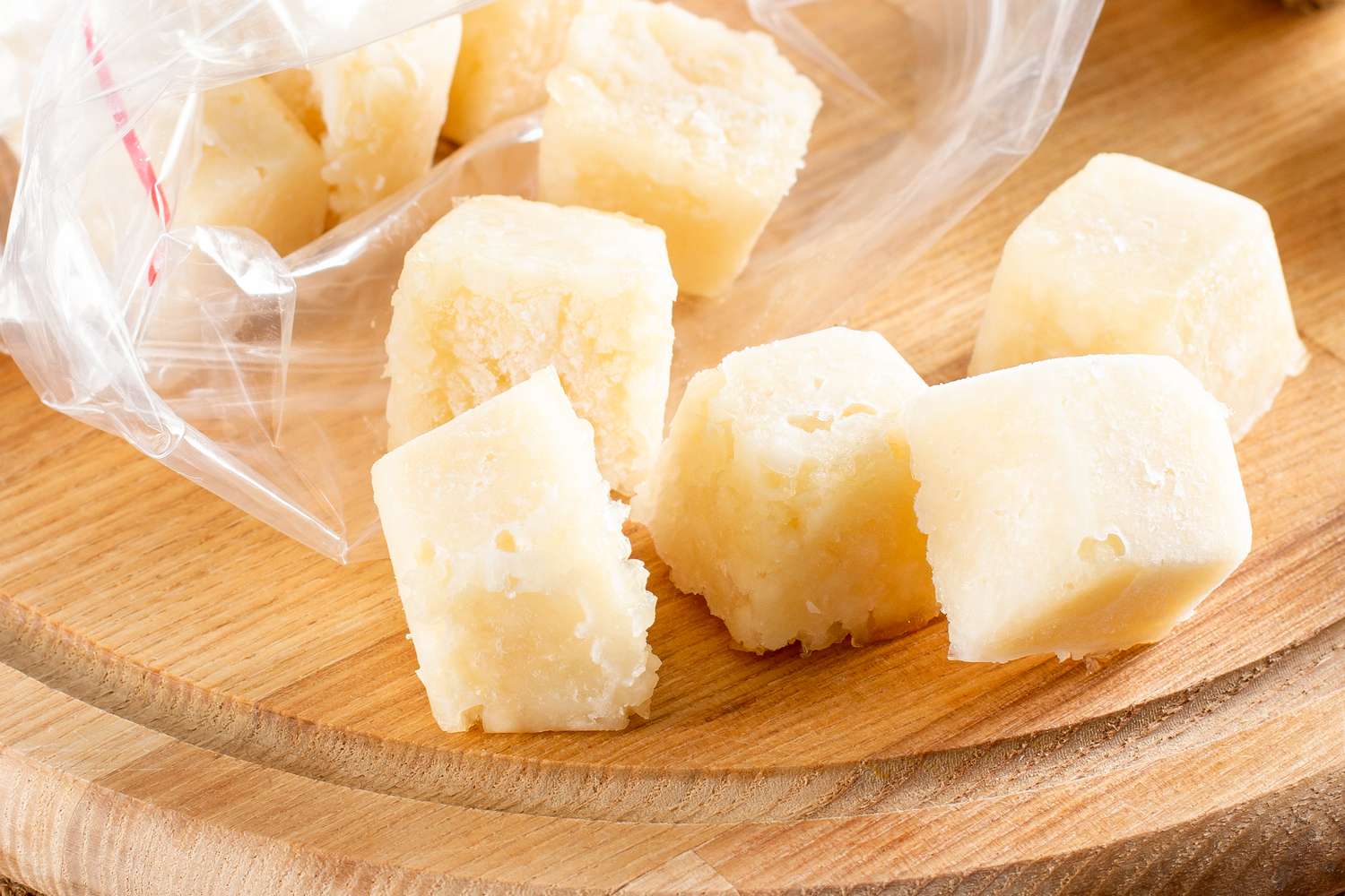 Cubes of frozen garlic on a wooden surface near a plastic bag