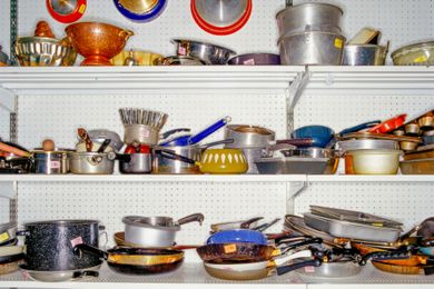 Shelves filled with assorted kitchen cookware and utensils in a thrift store setting
