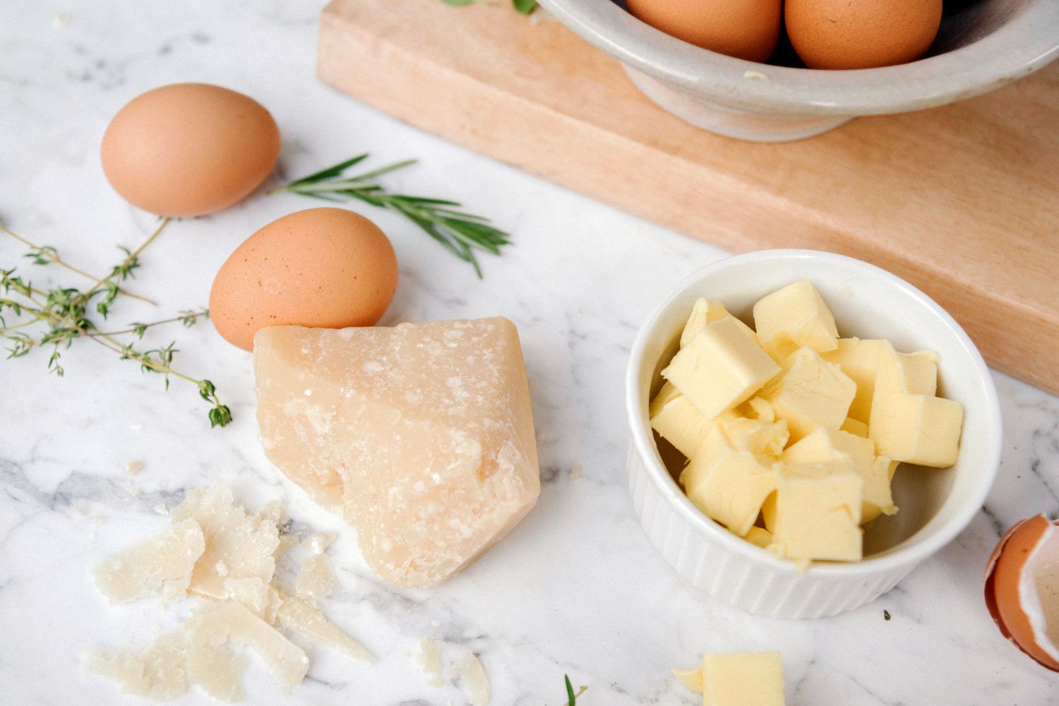 Eggs butter cubes a piece of cheese and herbs on a kitchen counter