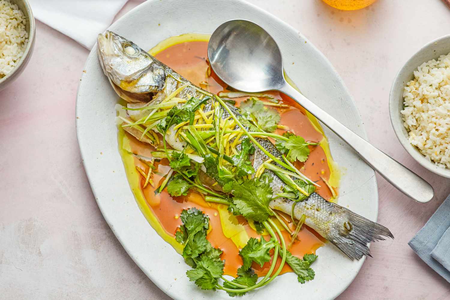 Overhead view of a steamed whole fish on a flatter and topped with sauce and herbs.