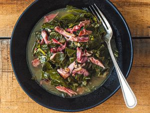 Overhead view of southern collard greens in a black bowl on a wood surface.