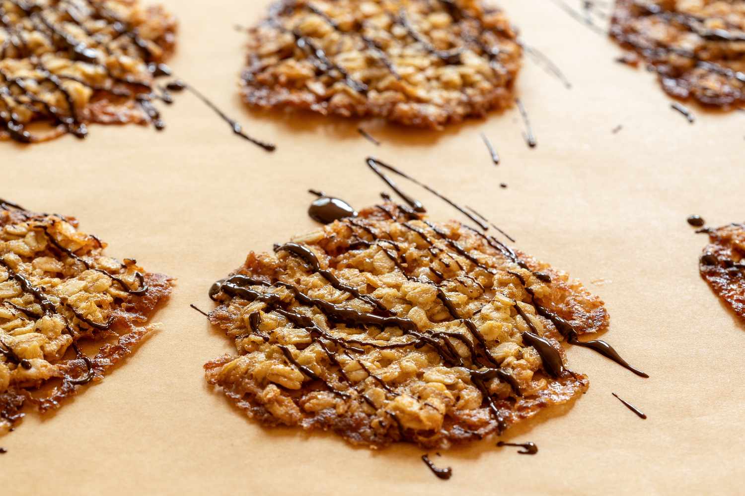 Oatmeal lace cookies drizzled with chocolate on a piece of parchment paper
