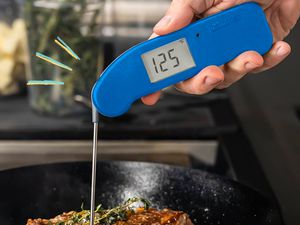 Thermapen thermometer measuring the temperature of steak cooking in a cast iron skillet