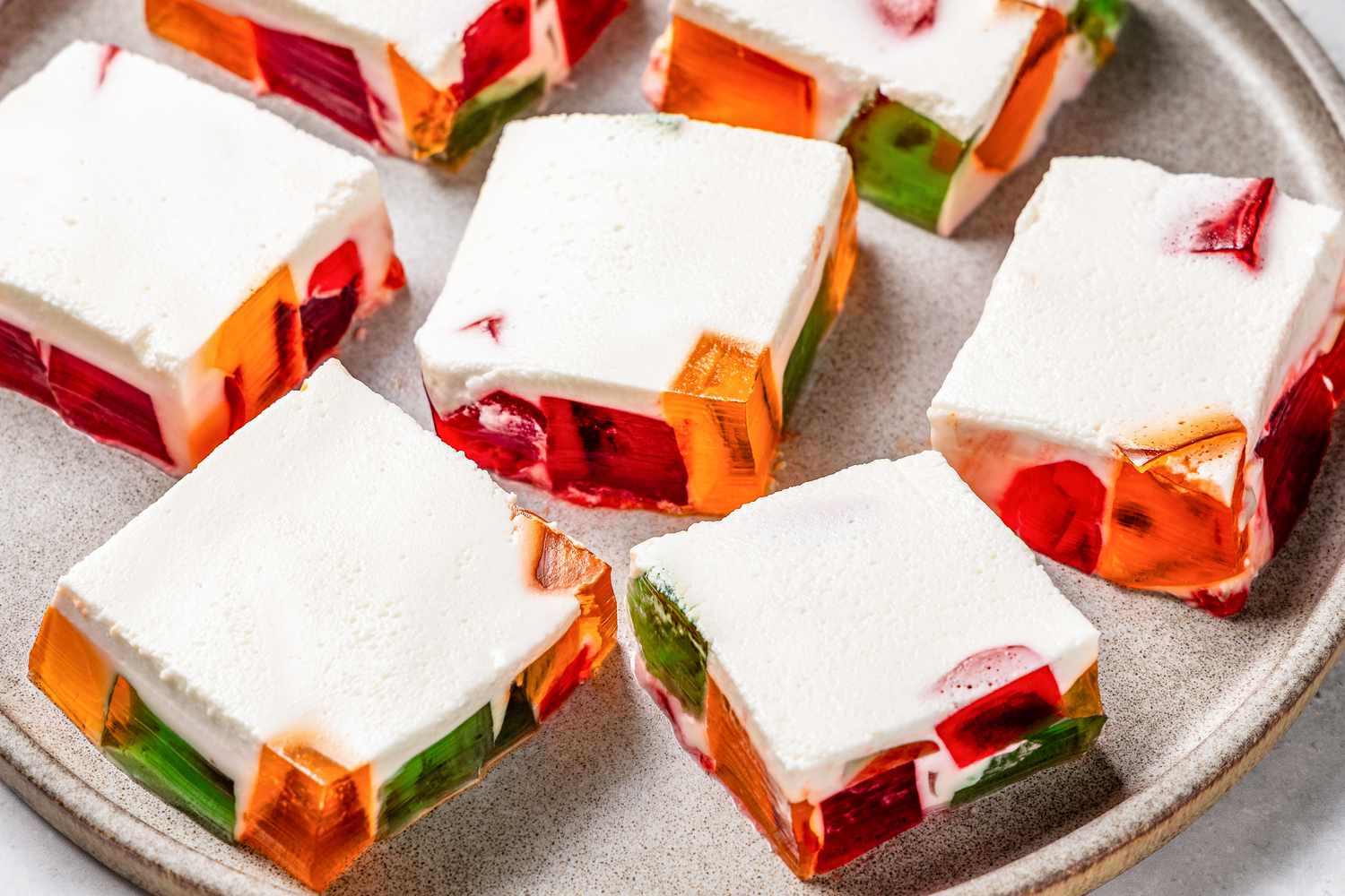 Squares of a dessert with colorful jelly pieces embedded in a creamy white base, arranged on a plate